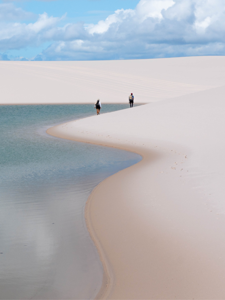 Dois caminhantes entre dunas e uma lagoa dos Lençóis Maranhenses